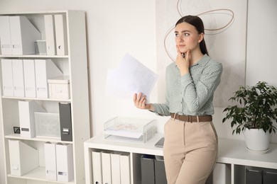 Embarrassed young woman with documents in office