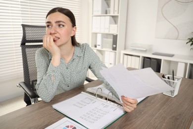 Photo of Embarrassed woman with documents at wooden table in office