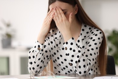 Photo of Embarrassed woman covering face with hands at table in office