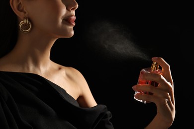 Photo of Woman spraying perfume on black background, closeup