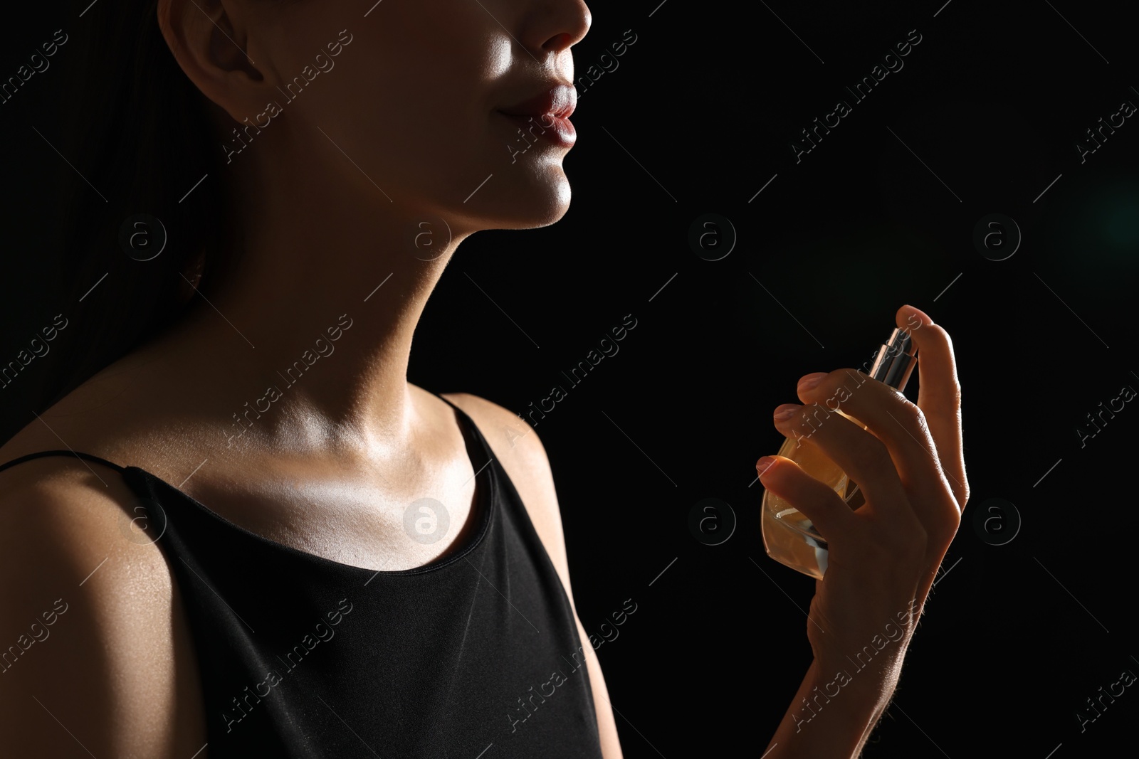 Photo of Woman spraying perfume on black background, closeup