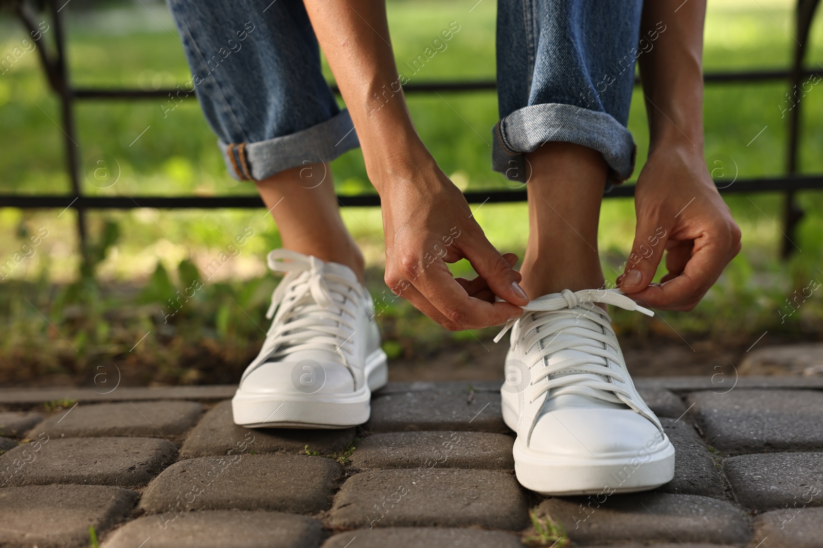 Photo of Woman tying shoelace of white sneaker outdoors, closeup