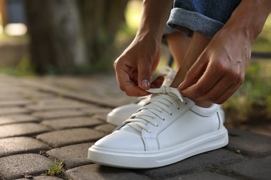 Photo of Woman tying shoelace of white sneaker outdoors, closeup. Space for text