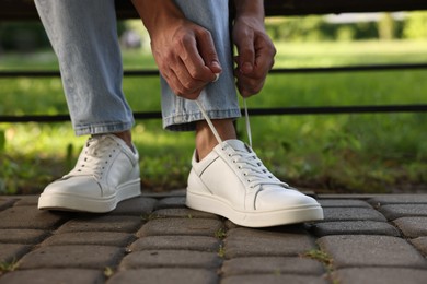 Photo of Man tying shoelace of white sneaker outdoors, closeup