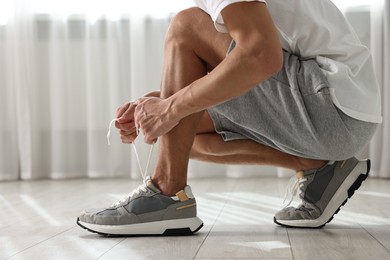 Photo of Man tying shoelace of sneaker indoors, closeup