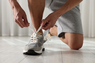 Photo of Man tying shoelace of sneaker indoors, closeup