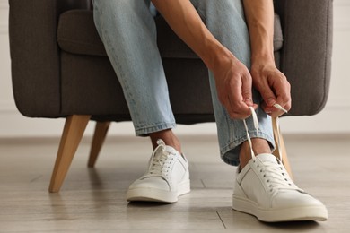 Photo of Man tying shoelace of sneaker indoors, closeup