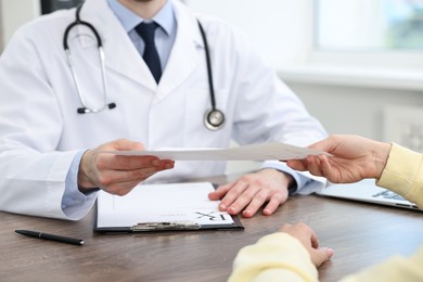 Photo of Doctor giving prescription to patient at wooden table in clinic, closeup