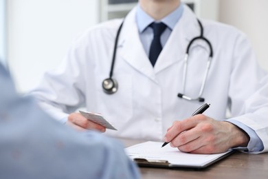 Photo of Doctor writing prescription for patient at wooden table in clinic, closeup