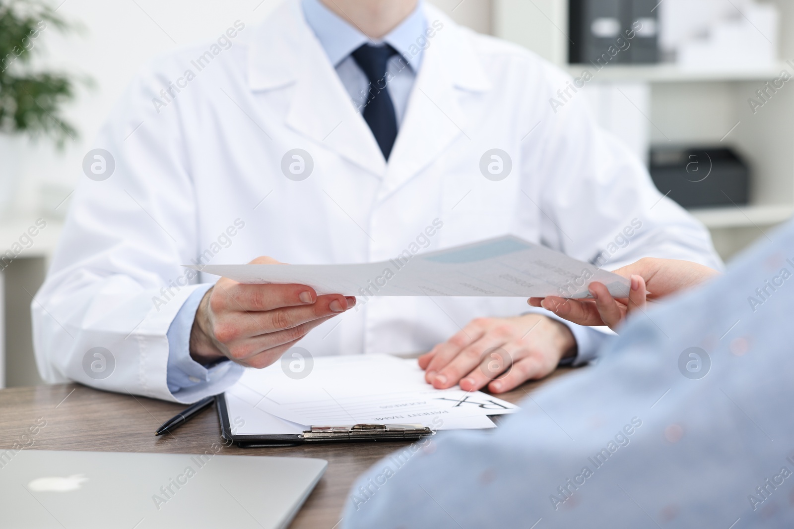 Photo of Doctor giving prescription to patient at wooden table in clinic, closeup