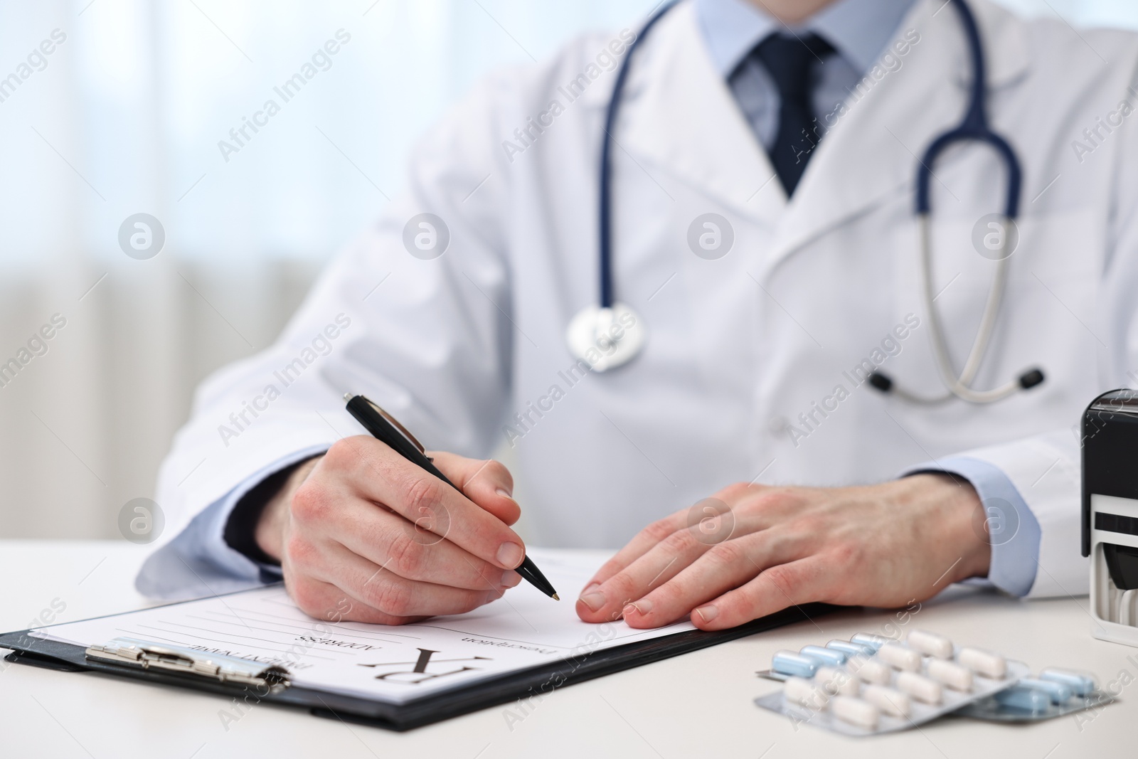 Photo of Doctor writing prescription at white table in clinic, closeup