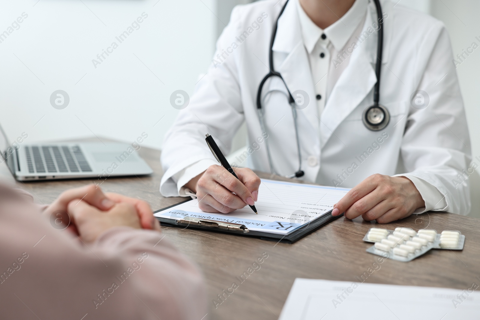 Photo of Doctor writing prescription for patient at wooden table in clinic, closeup