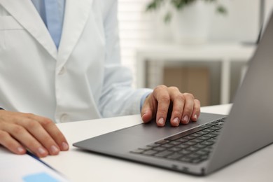 Photo of Doctor using laptop at white table in hospital, closeup