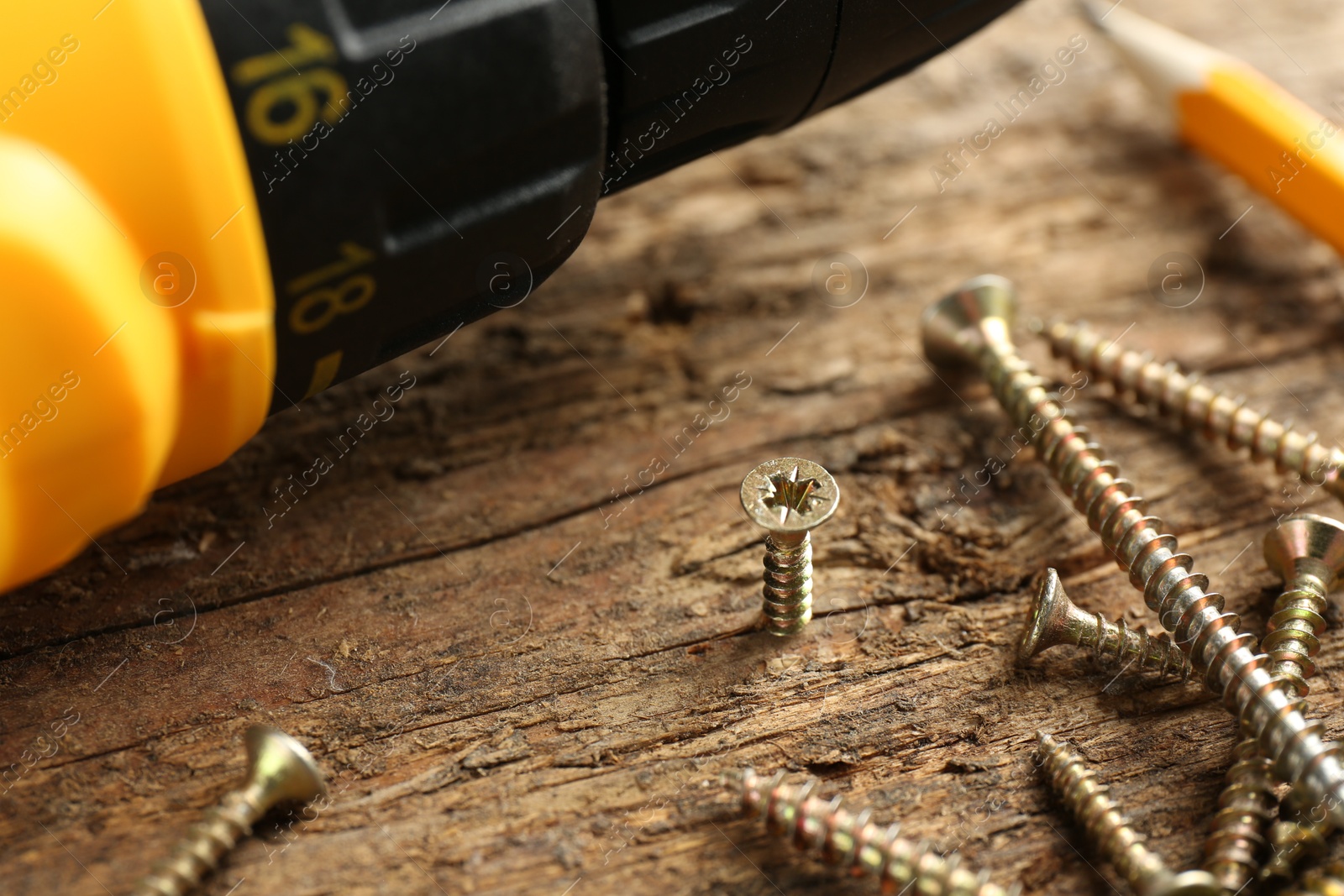 Photo of Electric screwdriver and screws on wooden plank, closeup