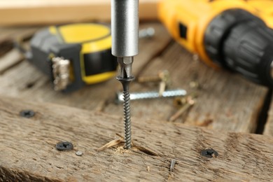 Photo of Screwing screw into wooden plank on table, closeup