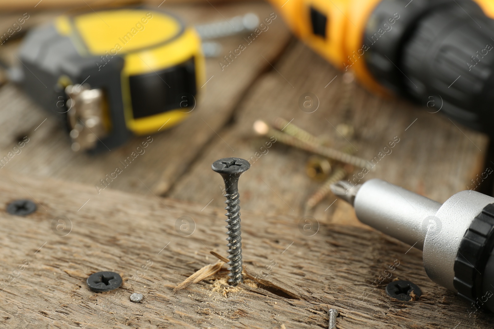 Photo of Screw in wooden plank and equipment on table, closeup