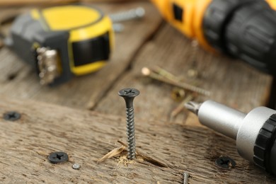 Screw in wooden plank and equipment on table, closeup