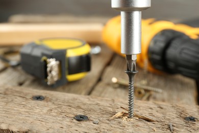 Photo of Screwing screw into wooden plank on table, closeup