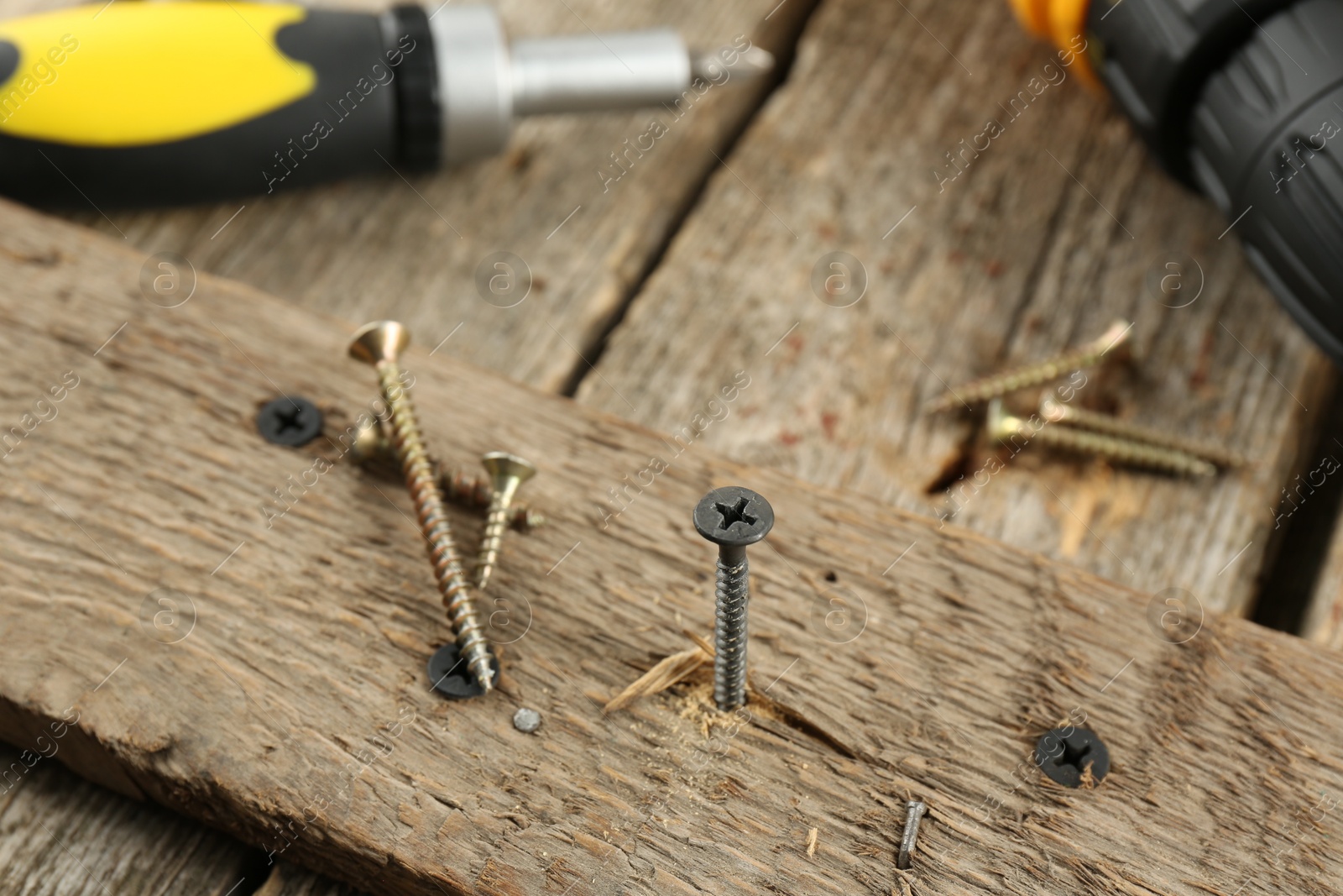 Photo of Screw in wooden plank and equipment on table, closeup