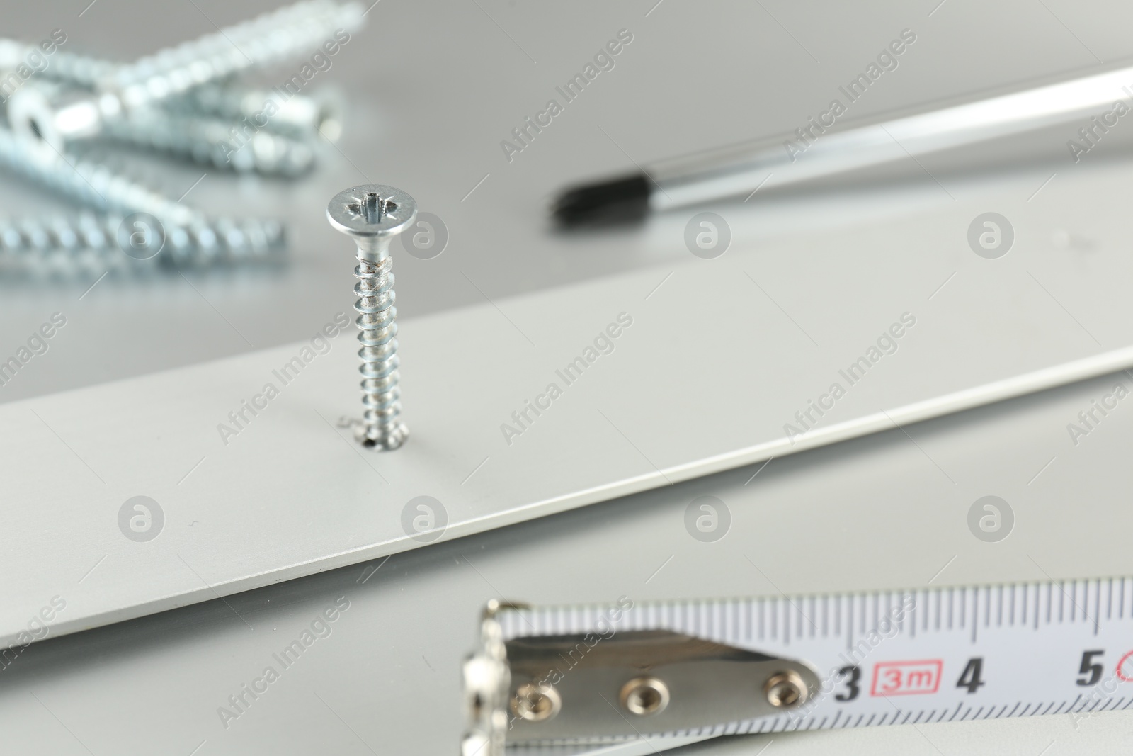 Photo of Metal screw in white panel and tools on light table, closeup