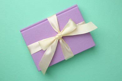 Photo of Book tied with beige ribbon on turquoise background, top view