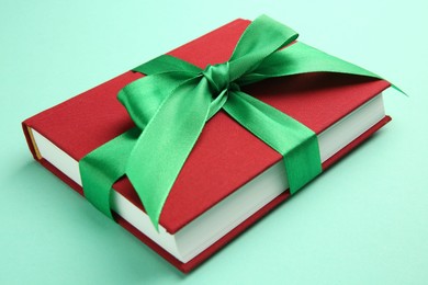 Photo of Book tied with green ribbon on turquoise background, closeup