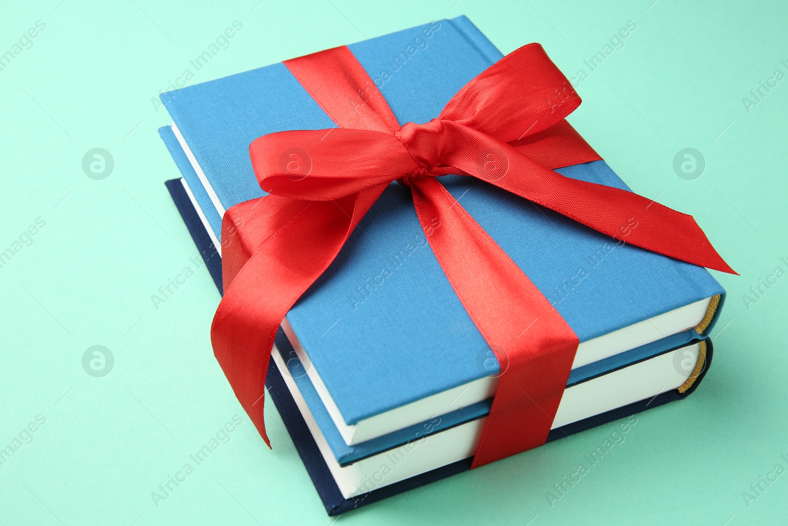 Photo of Books tied with red ribbon on turquoise background, closeup