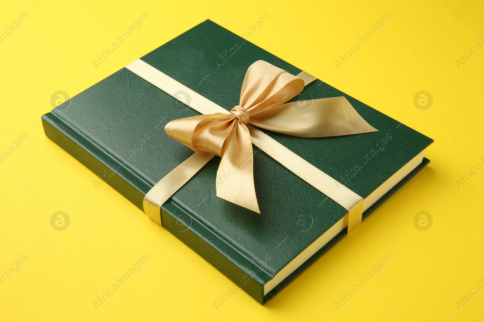 Photo of Book tied with golden ribbon on yellow background