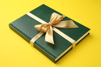 Photo of Book tied with golden ribbon on yellow background