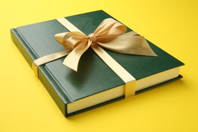 Book tied with golden ribbon on yellow background, closeup