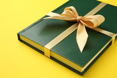 Book tied with golden ribbon on yellow background, closeup