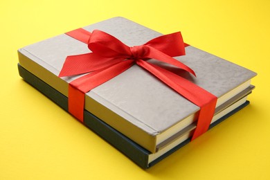 Photo of Books tied with red ribbon on yellow background, closeup