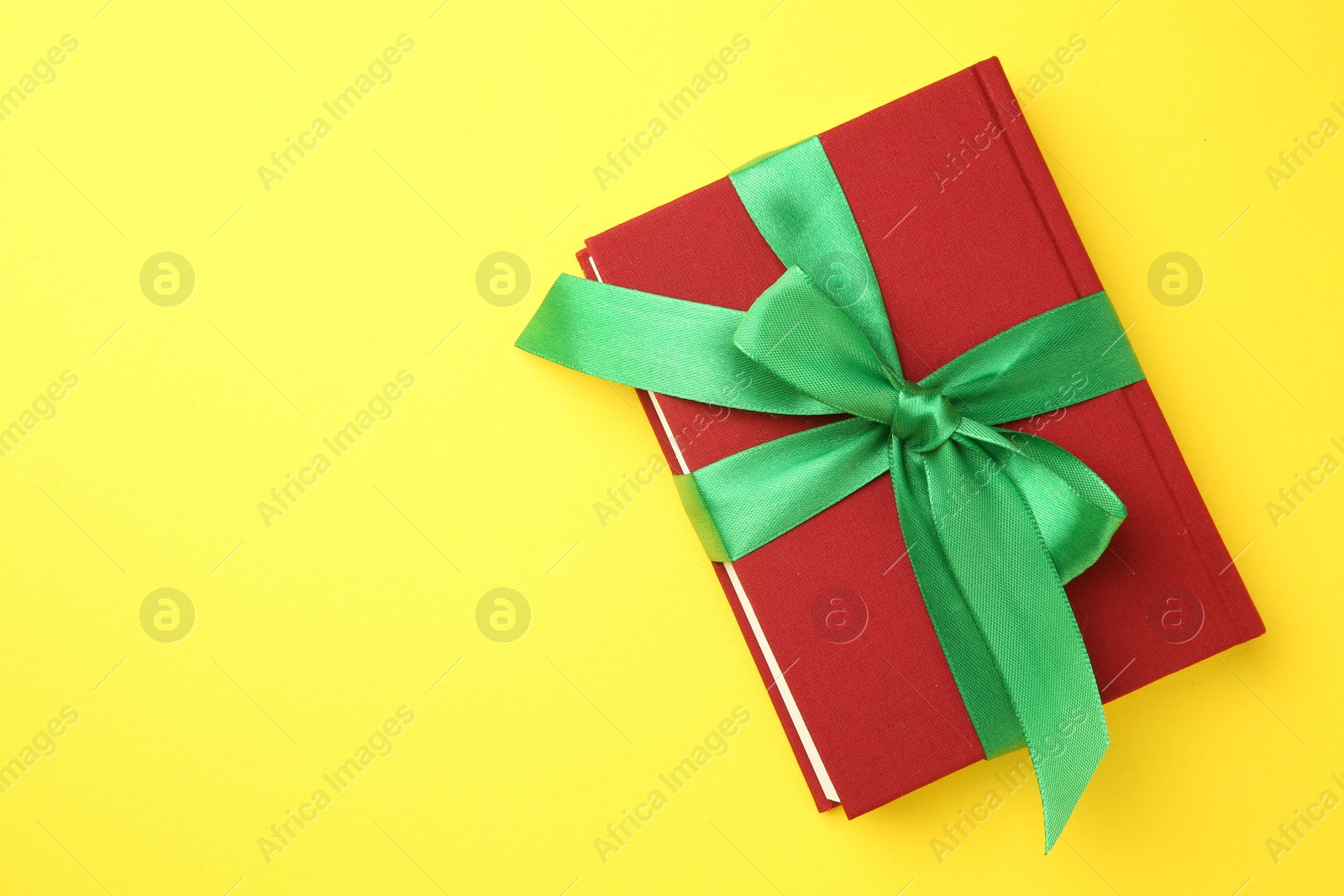 Photo of Book tied with green ribbon on yellow background, top view. Space for text