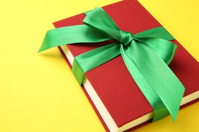 Photo of Book tied with green ribbon on yellow background, closeup. Space for text