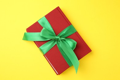 Book tied with green ribbon on yellow background, top view