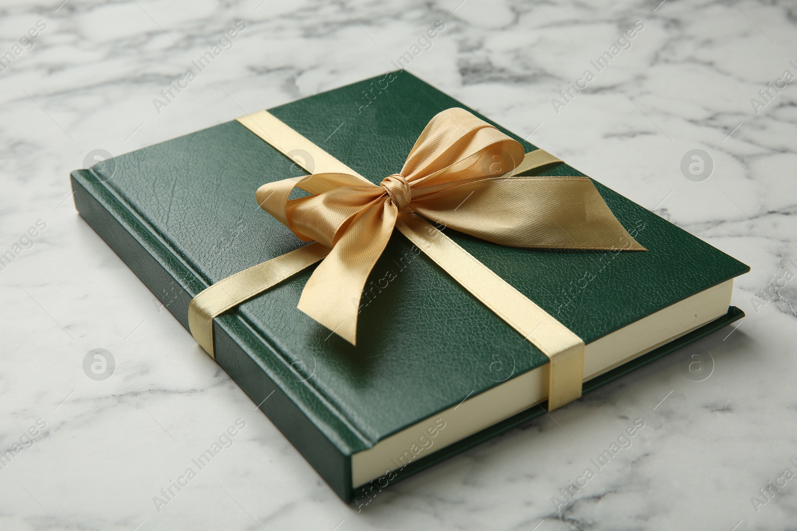 Photo of Book tied with golden ribbon on white marble table