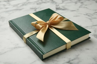 Photo of Book tied with golden ribbon on white marble table