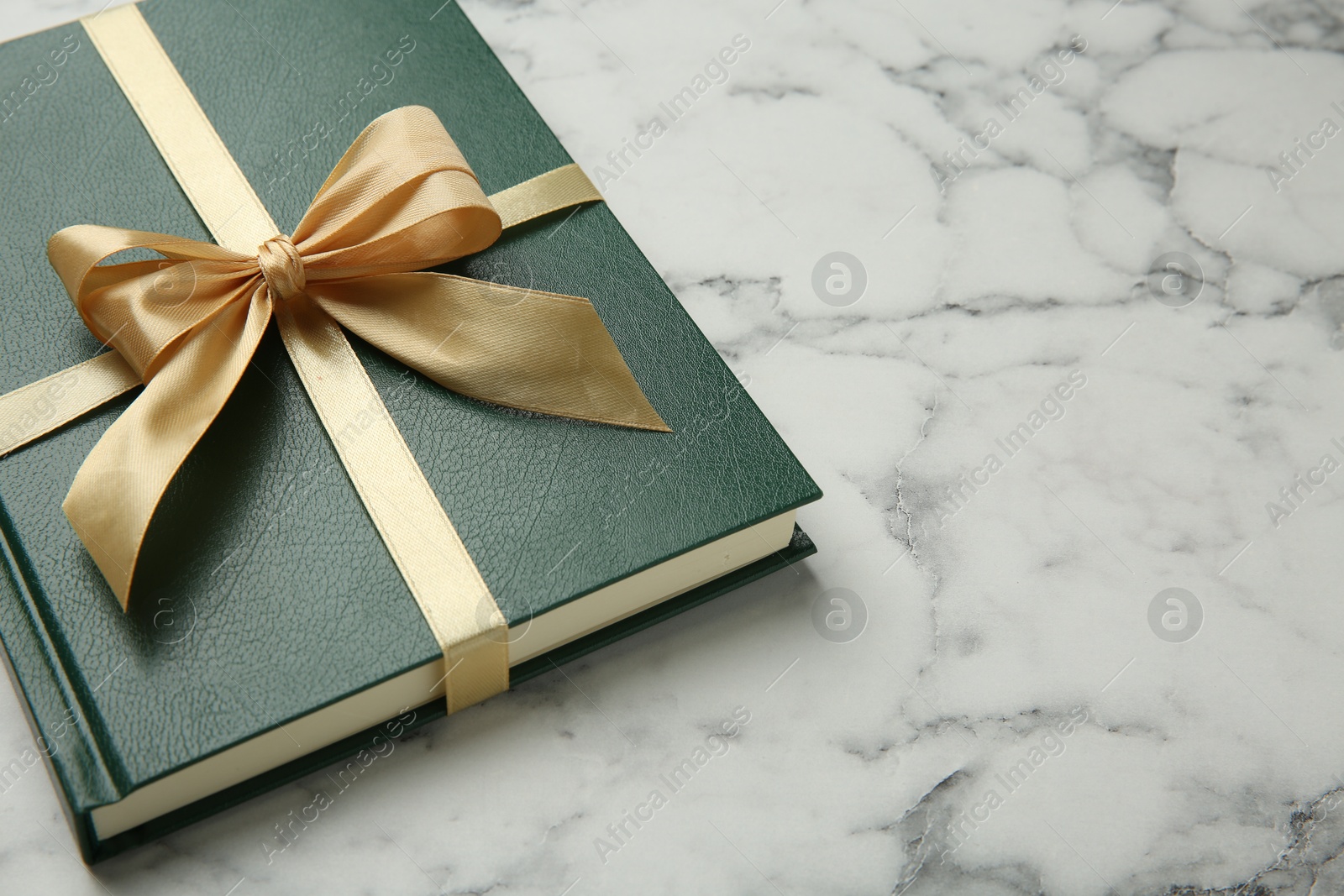 Photo of Book tied with golden ribbon on white marble table, space for text