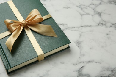 Book tied with golden ribbon on white marble table, space for text