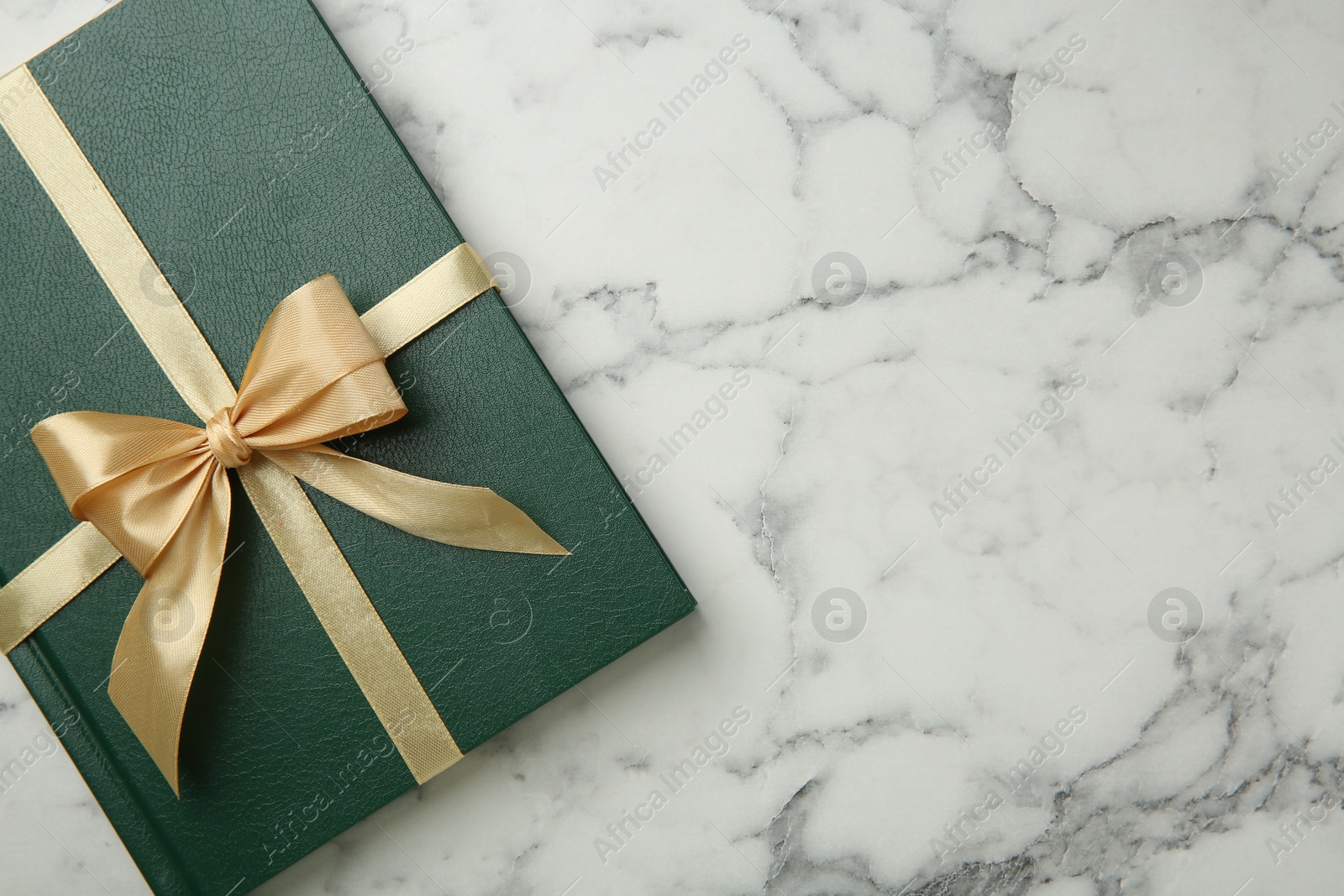 Photo of Book tied with golden ribbon on white marble table, top view. Space for text