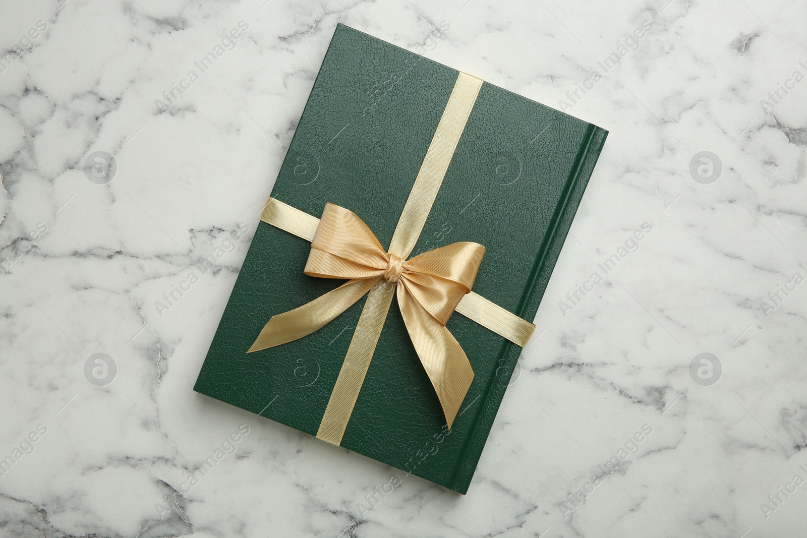 Photo of Book tied with golden ribbon on white marble table, top view