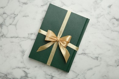 Book tied with golden ribbon on white marble table, top view