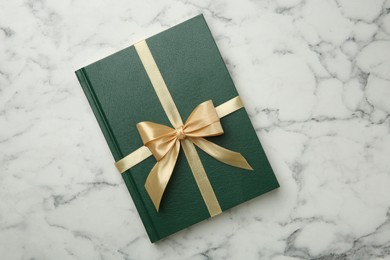 Photo of Book tied with golden ribbon on white marble table, top view