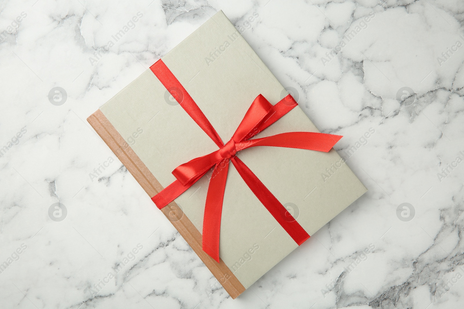 Photo of Book tied with red ribbon on white marble table, top view