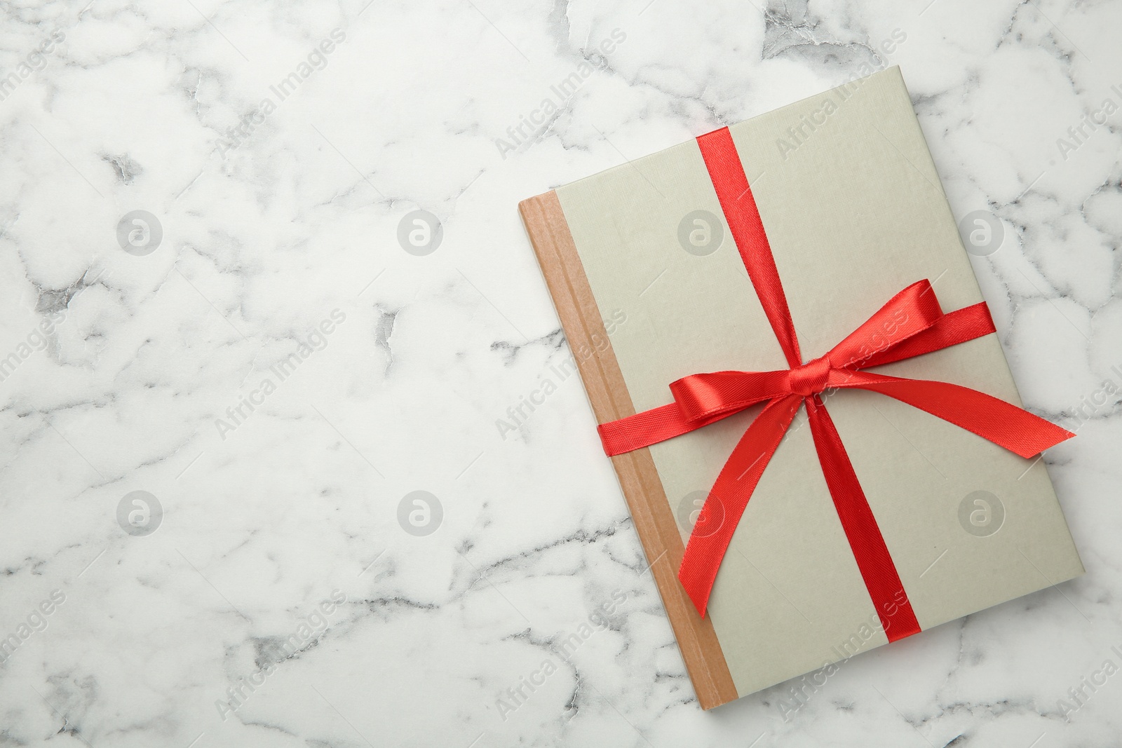 Photo of Book tied with red ribbon on white marble table, top view. Space for text