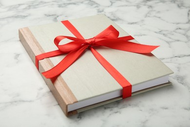 Photo of Book tied with red ribbon on white marble table