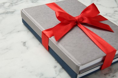 Photo of Books tied with red ribbon on white marble table, closeup. Space for text