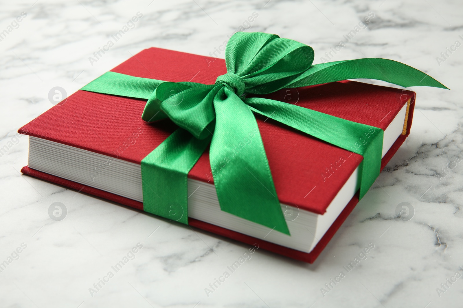 Photo of Book tied with green ribbon on white marble table, closeup