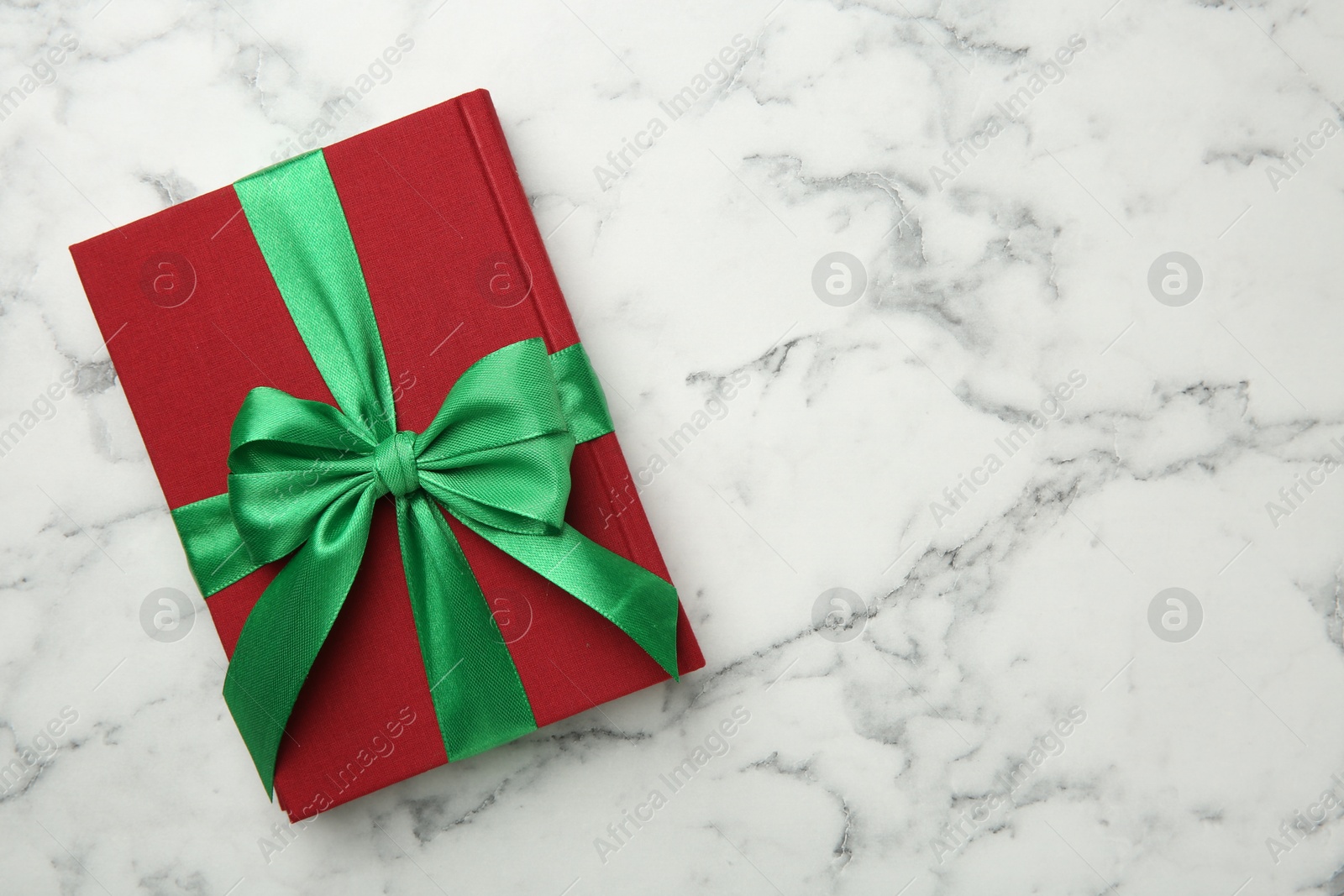 Photo of Book tied with green ribbon on white marble table, top view. Space for text