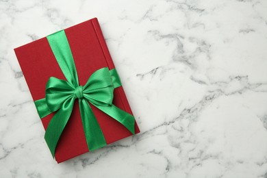 Photo of Book tied with green ribbon on white marble table, top view. Space for text